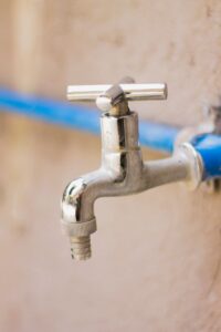 A close-up view of a shiny stainless steel faucet attached to a blue pipe on a wall.