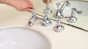 Close-up of a hand adjusting a chrome faucet in a modern bathroom interior.